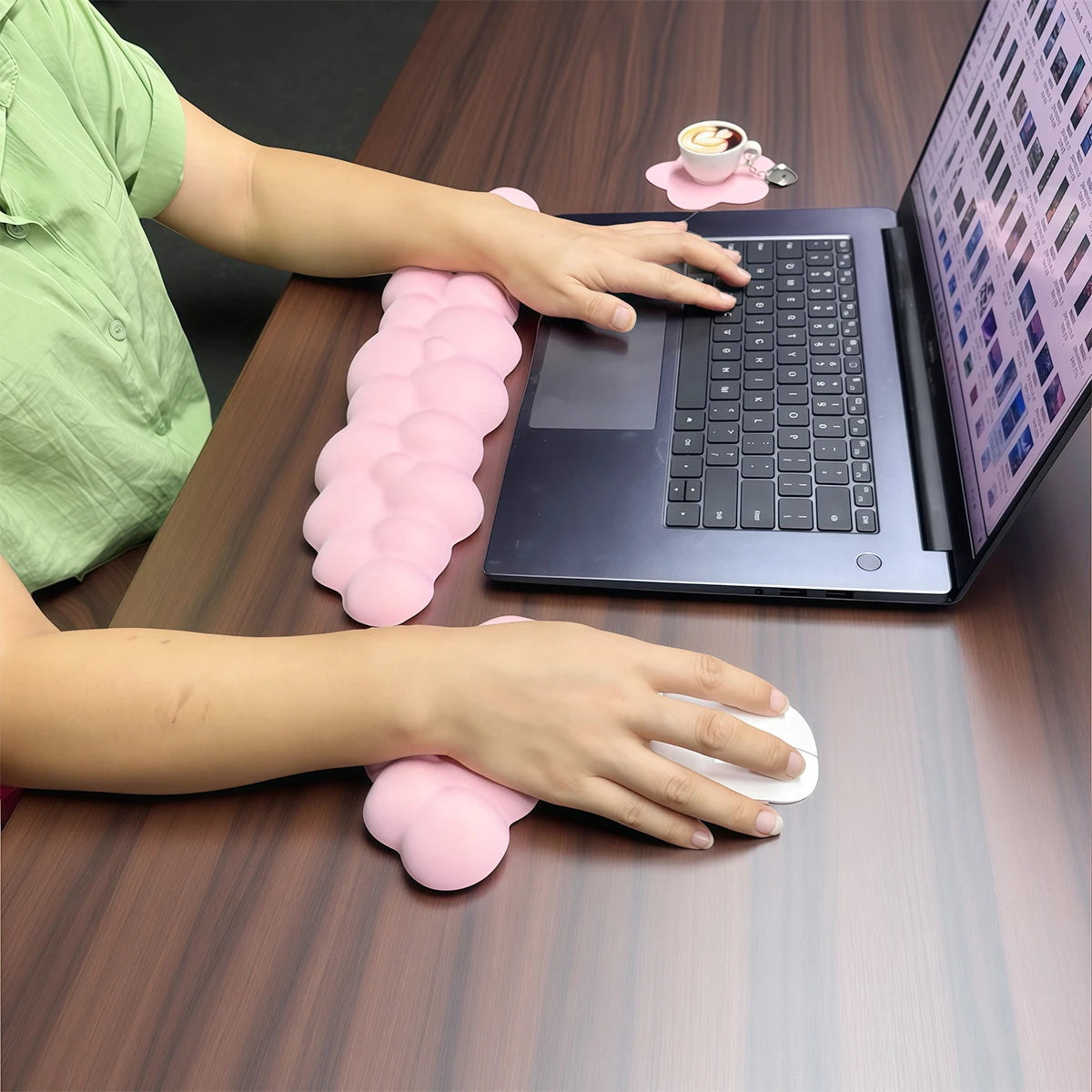 Une personne utilise un ordinateur portable avec un repose-poignet clavier nuage rose sur une table en bois.