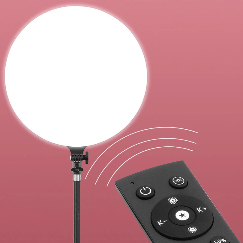 A round white LED ring light with a black base and control panel is shown against a pink background.