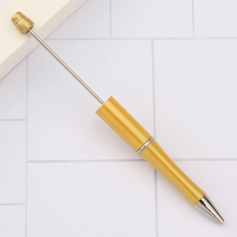 A gold-colored DIY beadable pen with a silver band and a pointed tip resting on a white surface.