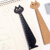 A black cartoon cat shaped wooden drawing ruler next to a natural wood ruler on a sheet of paper.