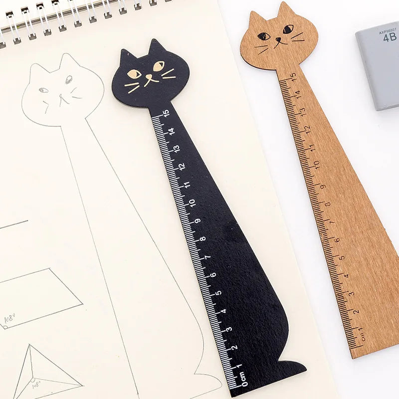A black cartoon cat shaped wooden drawing ruler next to a natural wood ruler on a sheet of paper.