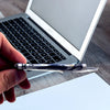 A hand holds an ultra-thin stainless steel money clip wallet next to a silver laptop.