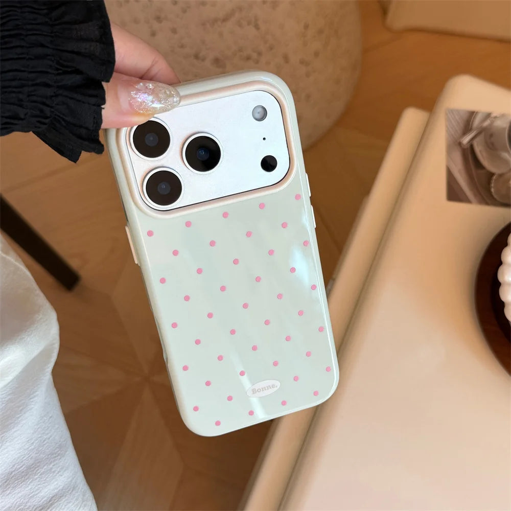 A light pink phone case with white polka dots is held by a hand, shown in a close-up shot.