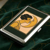 Vintage stainless steel card and cash case with a gold-toned illustration of a woman kissing a crescent moon on a dark green 