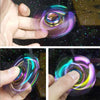 A hand is spinning a rainbow metal fidget spinner, showing vibrant iridescent colors.