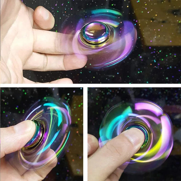 A hand is spinning a rainbow metal fidget spinner, showing vibrant iridescent colors.