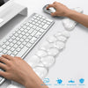 A hand is placing an ergonomic cloud wrist rest on a white desk next to a keyboard and mouse.