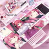 A pink anime character illustration on a mouse pad and desk mat with various stationery items.
