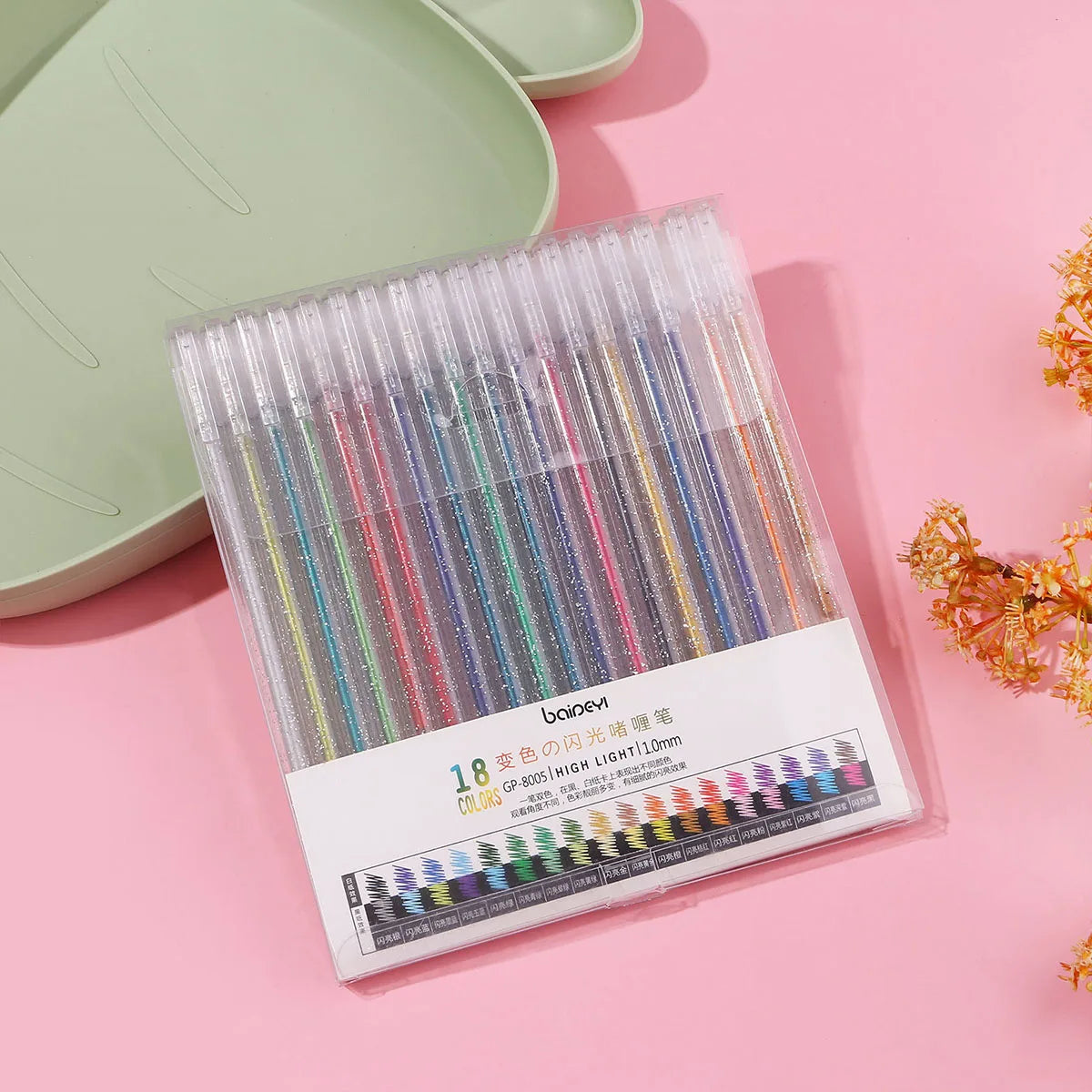 A clear plastic case filled with 18 colored glitter gel pens is displayed on a pink surface.