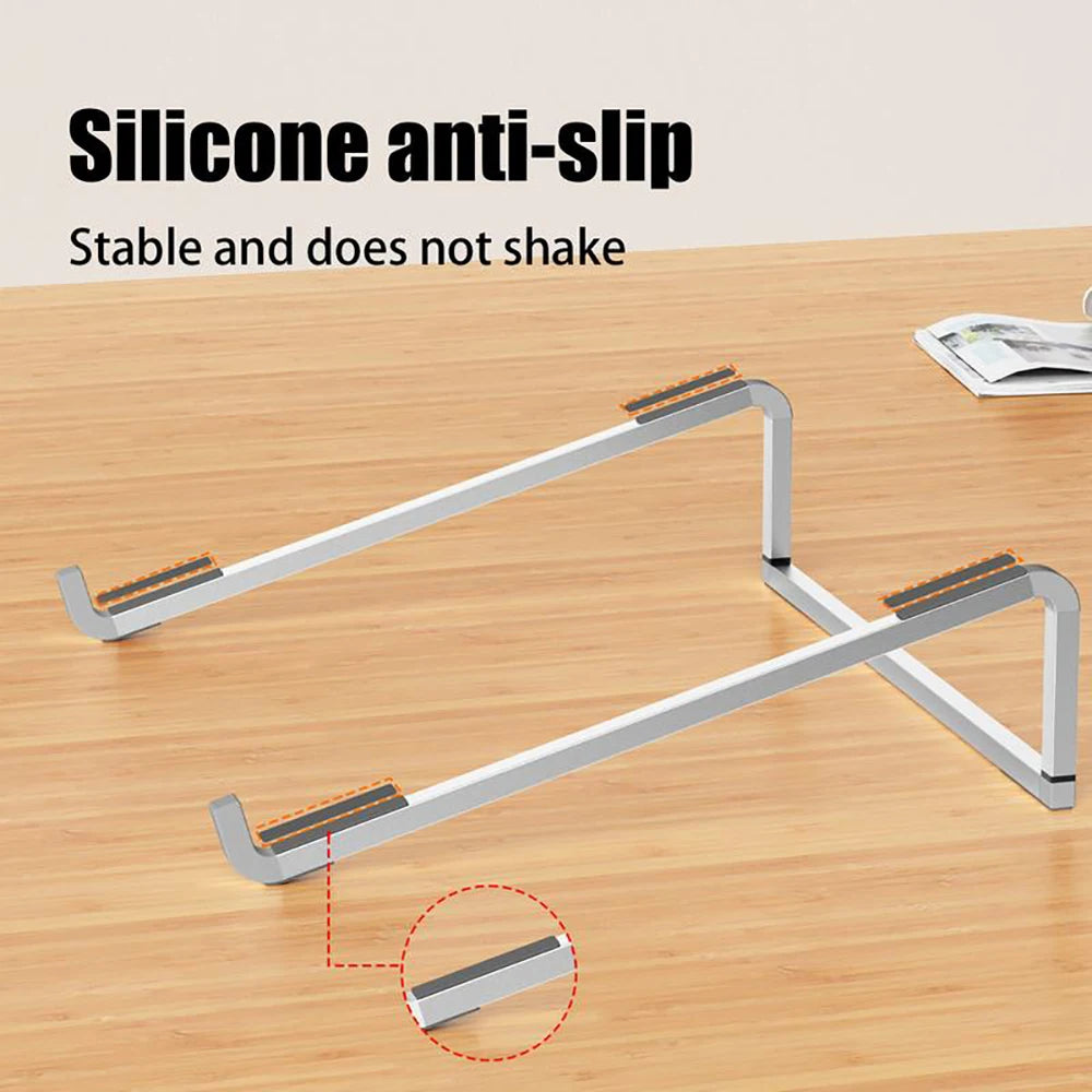 A silver foldable aluminum laptop stand with silicone anti-slip grips resting on a wooden table.