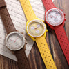 A collection of three perforated silicone watch straps in brown, yellow, and red laid on textured paper.
