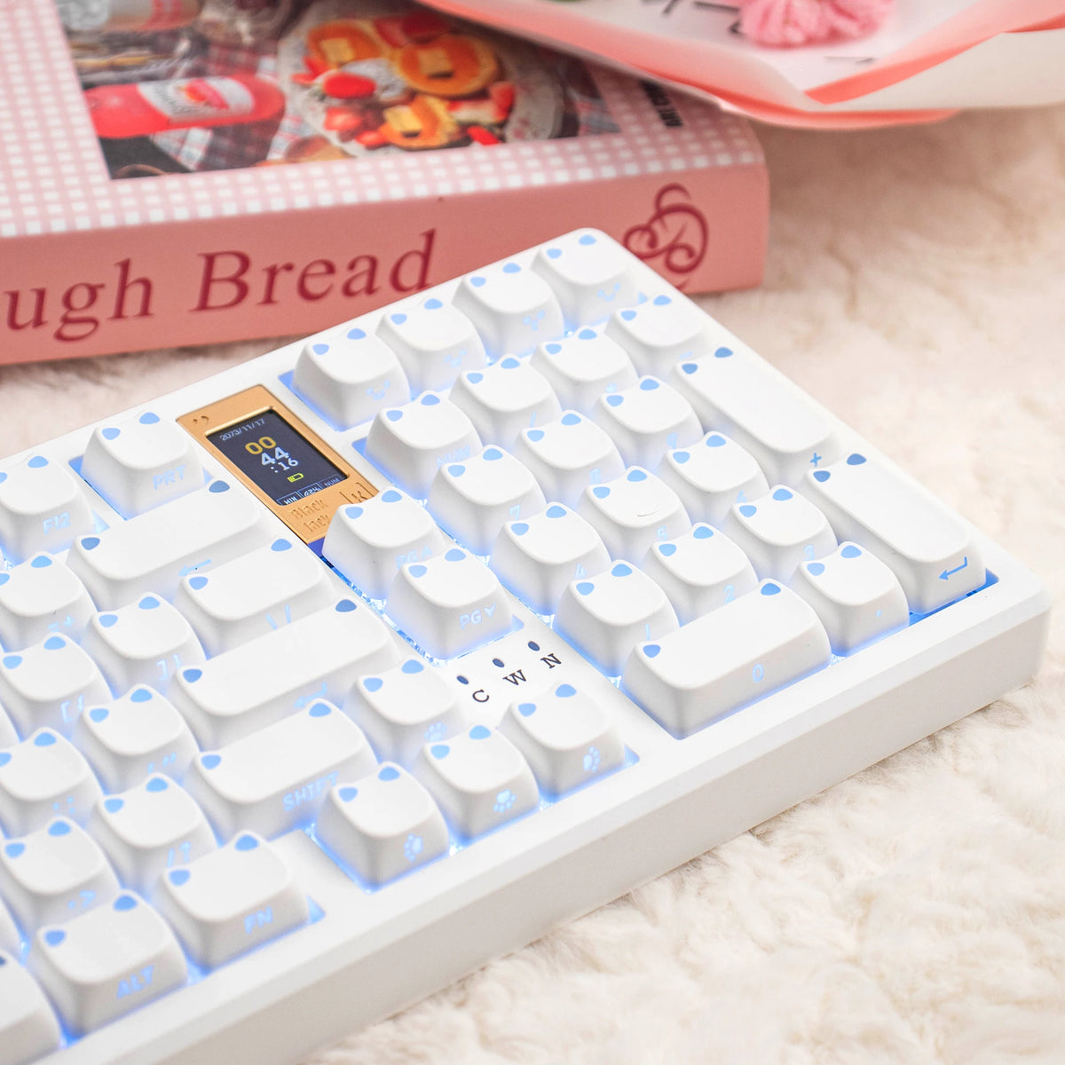 Eine weiße mechanische Tastatur mit hellblauen Tastenkappen neben einer rosa Box und Brot.