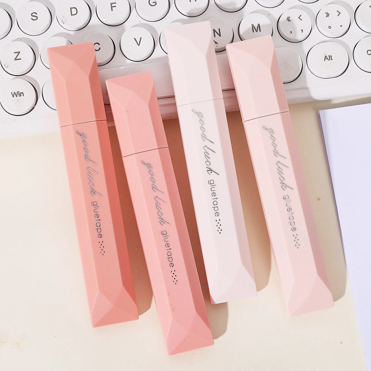 A set of pink gradient double-sided tape pens lying on a light surface next to a white keyboard.