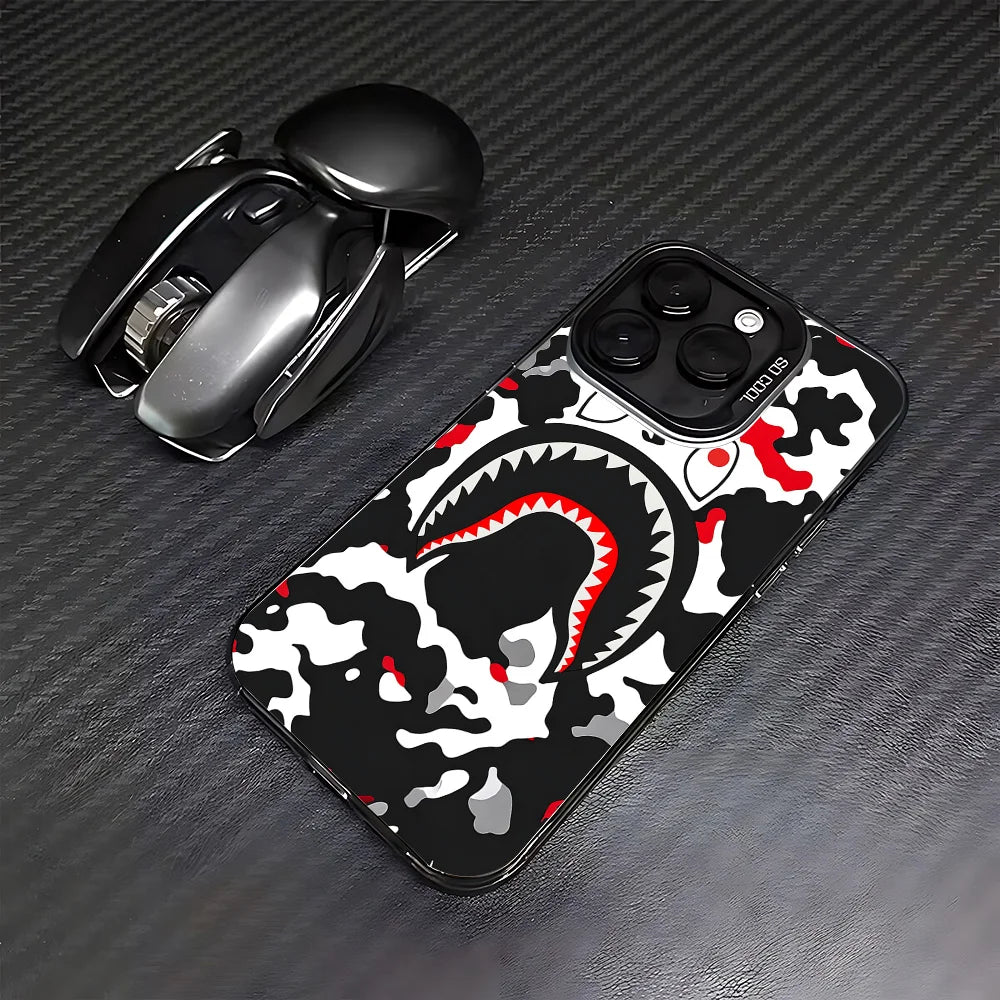 A black iPhone case featuring a white and red crocodile or shark pattern, placed next to the phone.