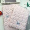 A pink quilted laptop sleeve with a checkered pattern is displayed next to a Kinfolk box.