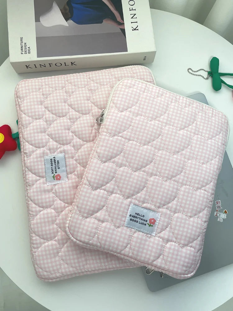 A pink quilted laptop sleeve with a checkered pattern is displayed next to a Kinfolk box.
