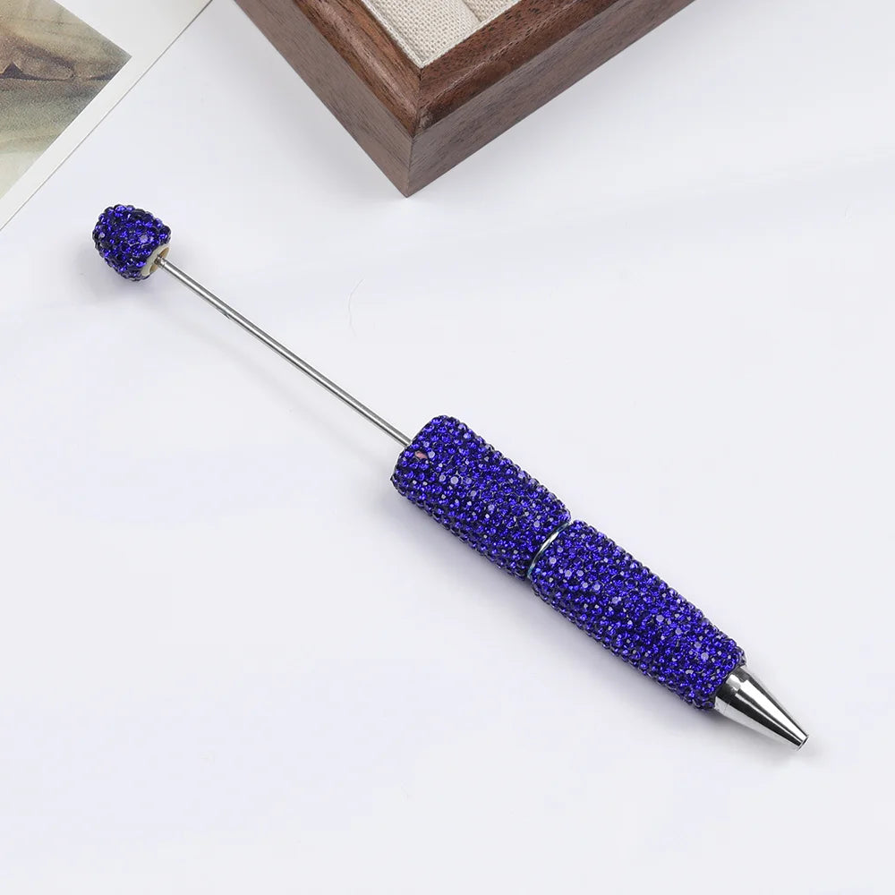 A silver pen accessory with a purple rhinestone bead on the tip and a body covered in purple beads.