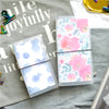 A transparent notebook shell with a pink floral pattern is displayed on a gray fabric surface.
