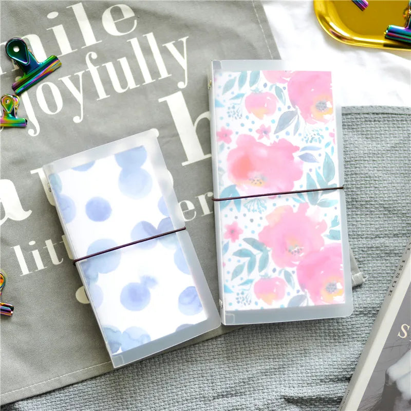 A transparent notebook shell with a pink floral pattern is displayed on a gray fabric surface.
