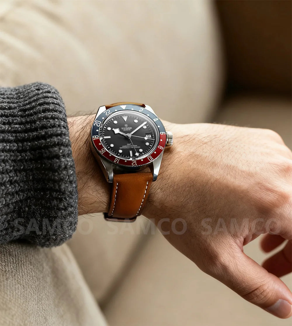 A close-up of a men's watch with a stainless steel case and brown leather band worn on a wrist.