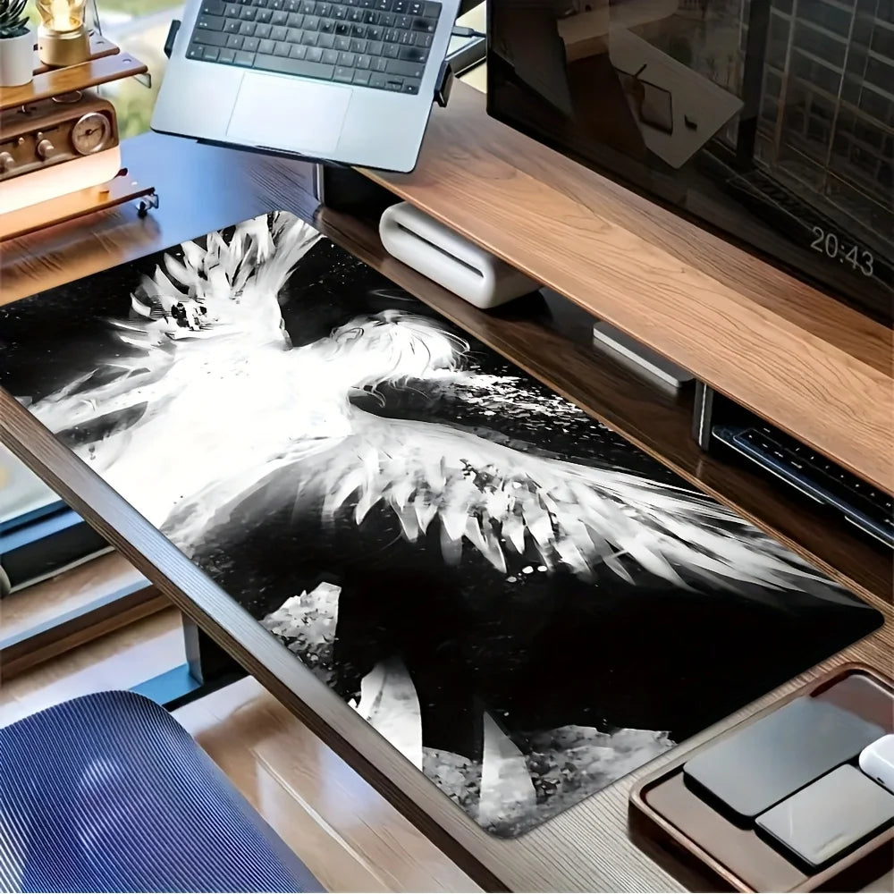 A black and white artistic angel wing desk mat mouse pad is displayed on a wooden desk next to a laptop.