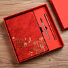 A red box containing a luxury PU leather notebook and a pen set with gold accents on a wooden surface.