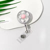 A clear retractable ID badge holder with a floral pull buckle and pink charm resting on a white plate.