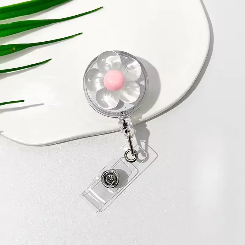 A clear retractable ID badge holder with a floral pull buckle and pink charm resting on a white plate.