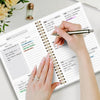 A hand is writing in an undated weekly planner notebook with habit trackers and appointments.