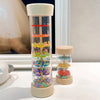 A clear plastic tube filled with colorful beads and rings, mounted on a wooden base, used as a musical instrument.