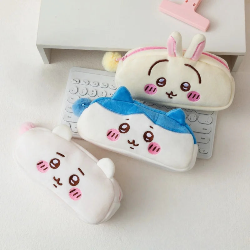 A collection of Chiikawa plush pencil cases and organizers in white, pink, and blue colors resting on a white desk.
