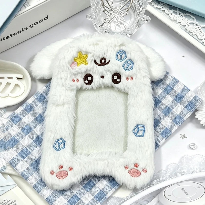 A white plush photocard holder with a soft cover featuring cute star and cube decorations, resting on a checkered cloth.