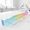 A colorful straight-edge geometric drawing cube is laid across a blueprint on a white desk.