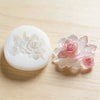 A set of pressed flower wax seals in pale pink and white on a wooden surface.