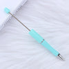 A silver and turquoise DIY beadable pen is shown lying on a white, fluffy surface.