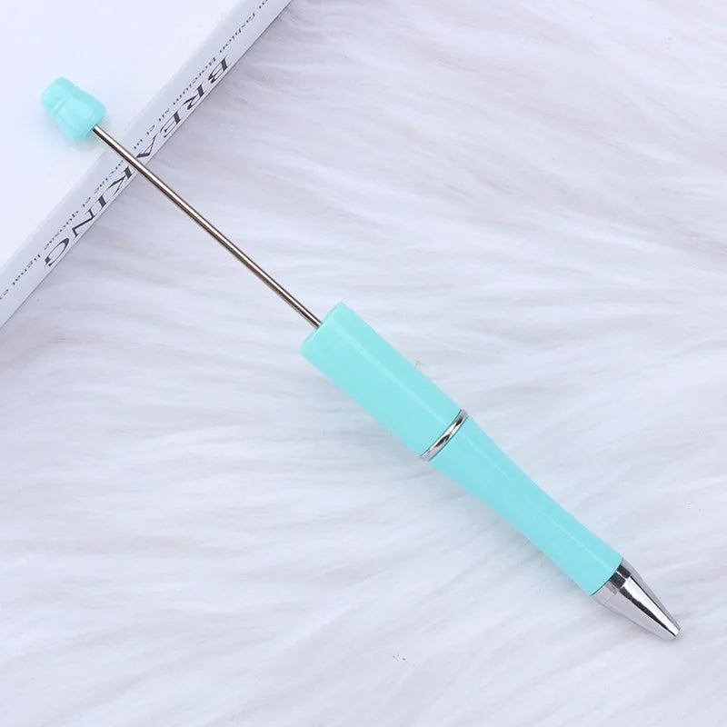 A silver and turquoise DIY beadable pen is shown lying on a white, fluffy surface.
