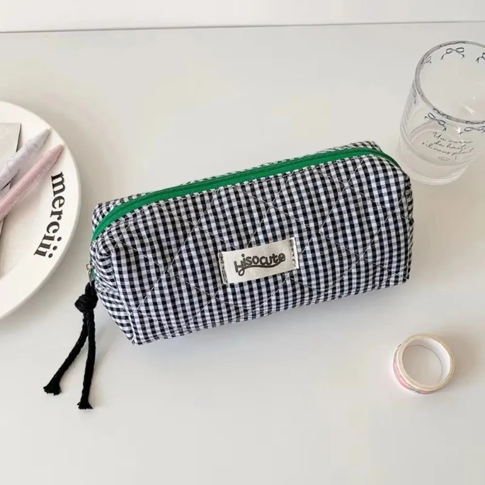 A black and white checkered pencil case with a green trim resting on a white surface.