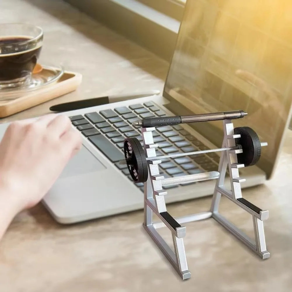 A silver barbell rack desk pen holder organizer is placed next to an open laptop on a light surface.