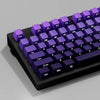 A close-up view of a mechanical keyboard with purple gradient keycaps and black casing.