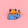 An enamel pin featuring a frog wearing a blue shirt with a patriotic design making a peace sign.