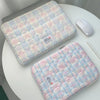 A pink and blue plaid quilted laptop sleeve resting on a white table next to a white wireless mouse.