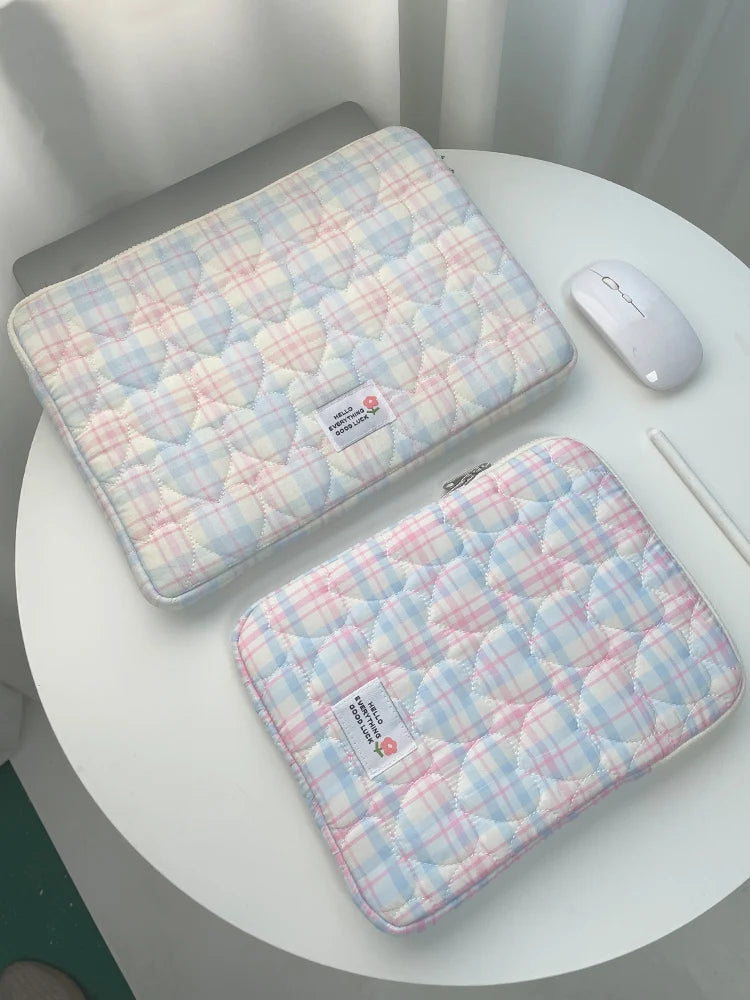 A pink and blue plaid quilted laptop sleeve resting on a white table next to a white wireless mouse.