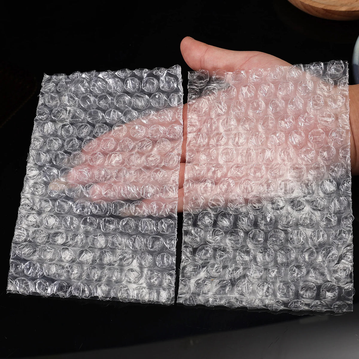 A hand is holding a sheet of transparent bubble wrap padded shipping bags.