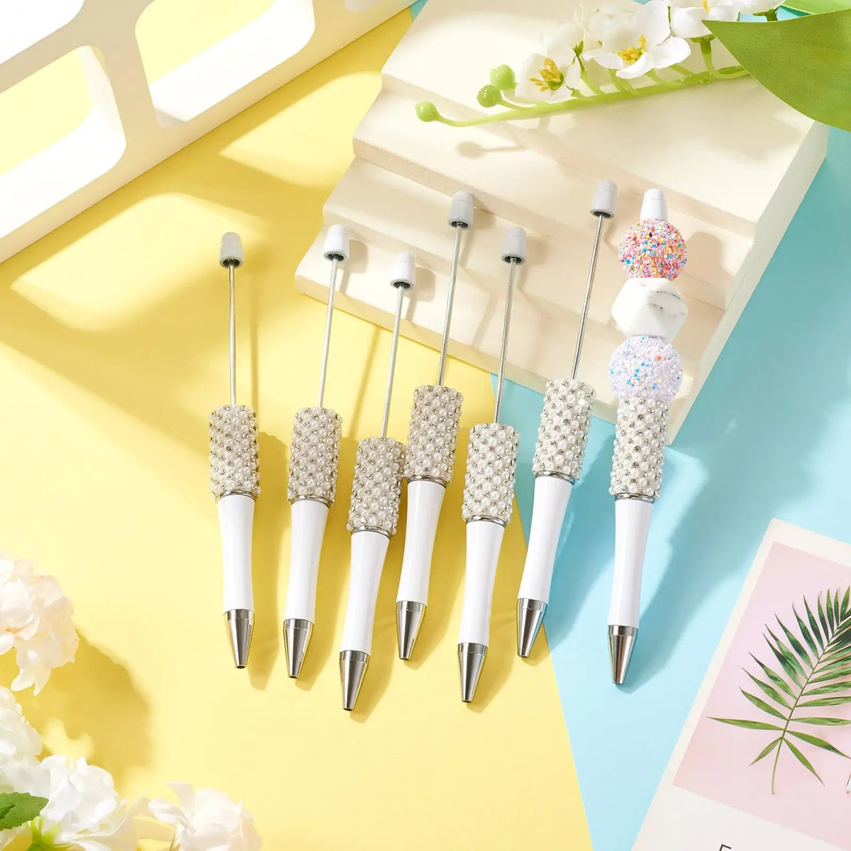 A set of pearl beaded ballpoint pens displayed on a light wooden surface with soft lighting.