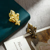 Two gold iris-shaped metal binder clips resting on a light surface next to a dark teal object.