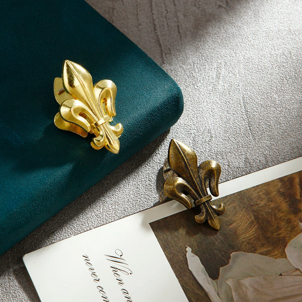Two gold iris-shaped metal binder clips resting on a light surface next to a dark teal object.