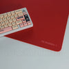 A close-up view of a pink and black mechanical keyboard resting on a red desk mat.