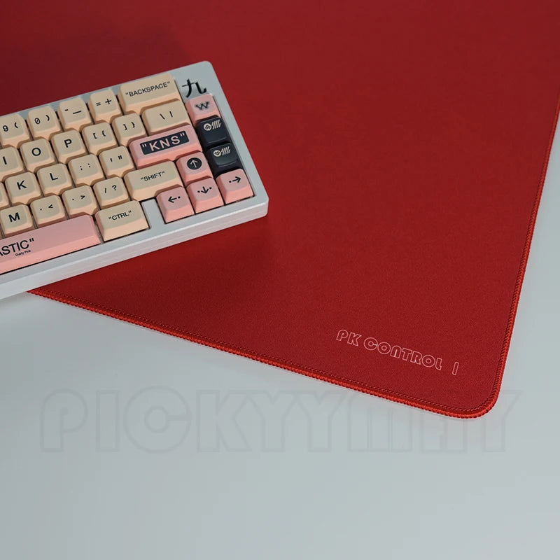 A close-up view of a pink and black mechanical keyboard resting on a red desk mat.