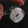 A hand is peeling off a roll of clear double-sided nano tape for household repair.