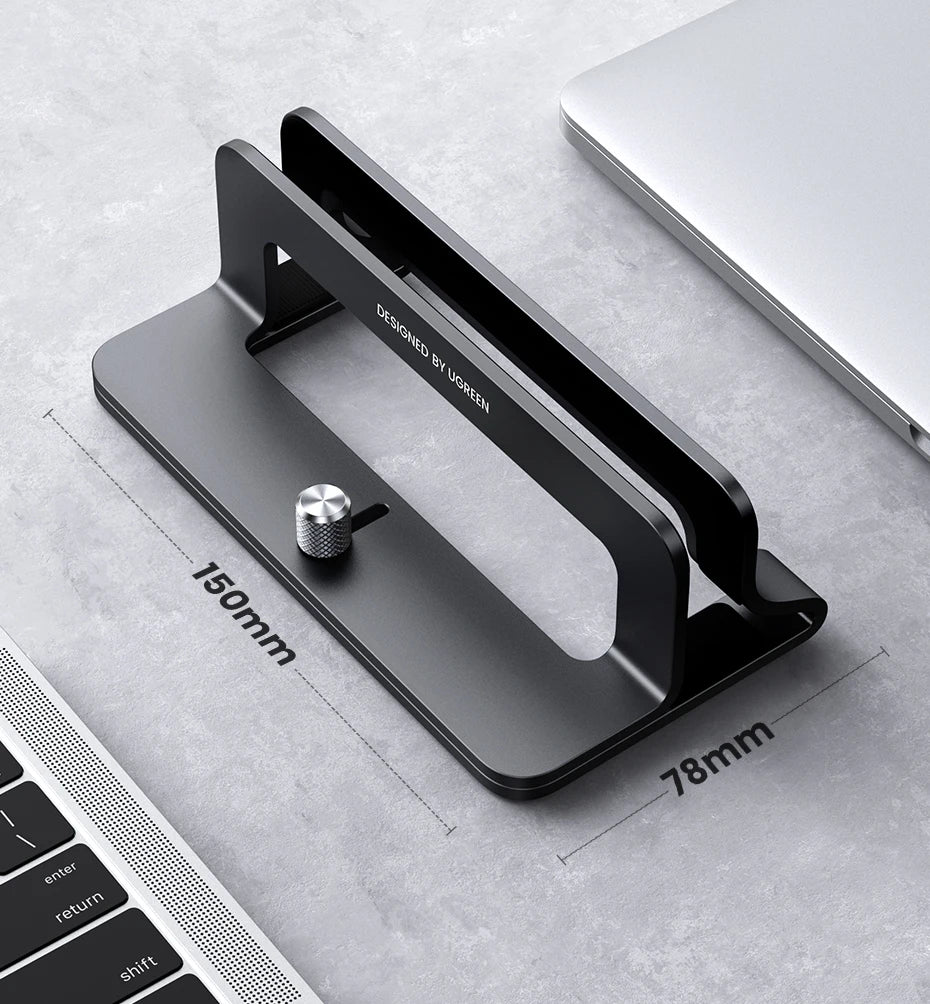 A black vertical laptop stand designed by Ugreen shown on a gray surface next to a laptop keyboard.